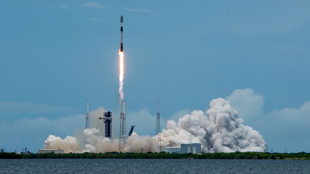 a black-and-white spacex falcon 9 rocket launches into a blue sky.