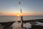 a large silver rocket comes back to earth to land beside its launch tower, with the rising sun and the ocean in the background