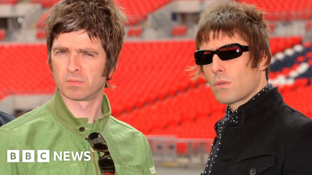 Noel and Liam Gallagher frowning at the camera in a photo taken in 2008. Noel is wearing a green jacket and Liam a black one. He is wearing sunglasses. Both have mod hairstyles.