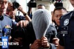 A man linked to Global Ikhwan Service and Business Holdings (GISB) covers his face as he is escorted by police officers after being charged in a court in Putrajaya, Malaysia September 18, 2024.